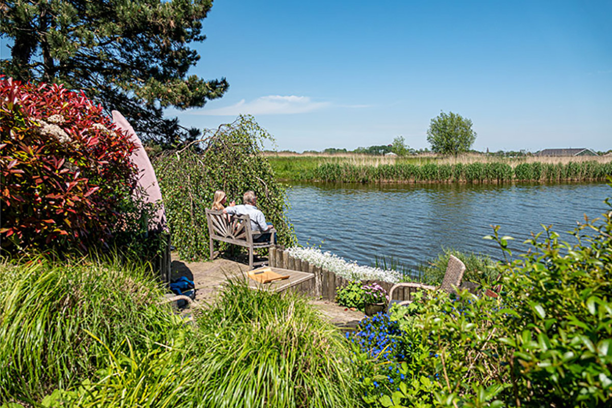 Zonnige tuin met terrasje aan het water.