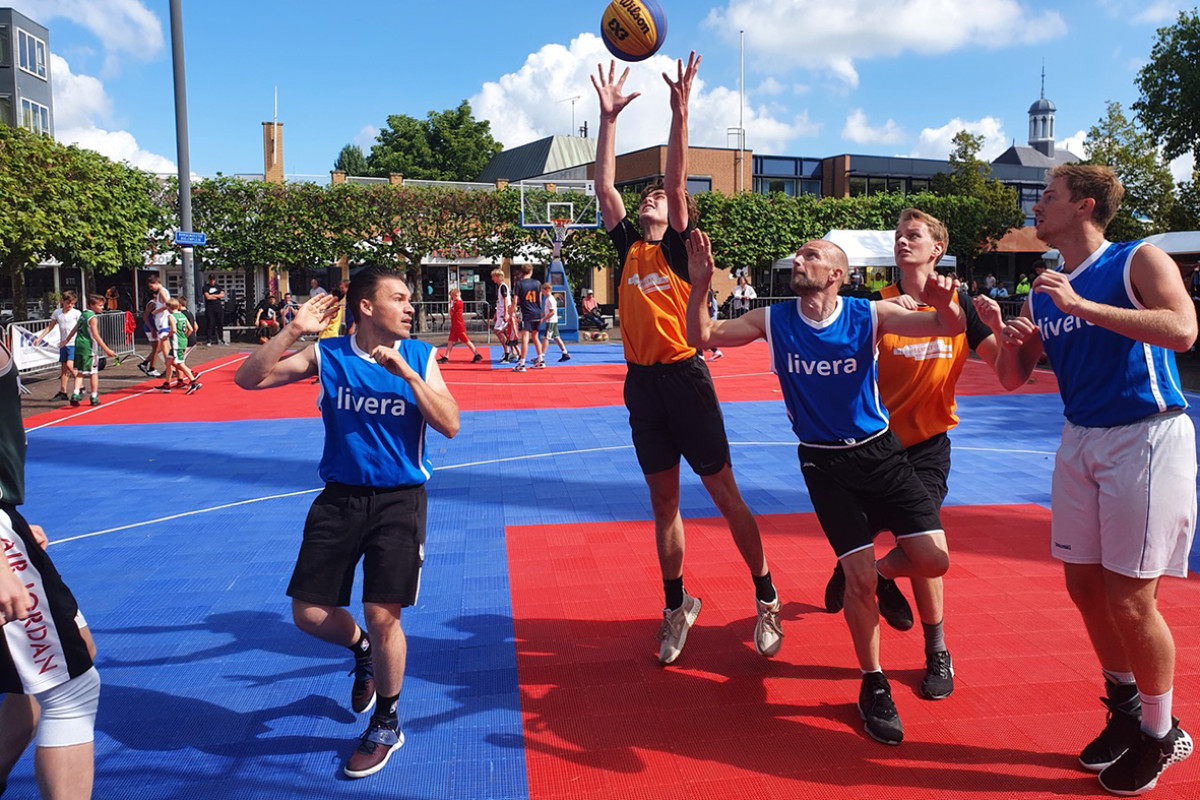 Jongens spelen buiten basketbal op een rood-blauw veld.