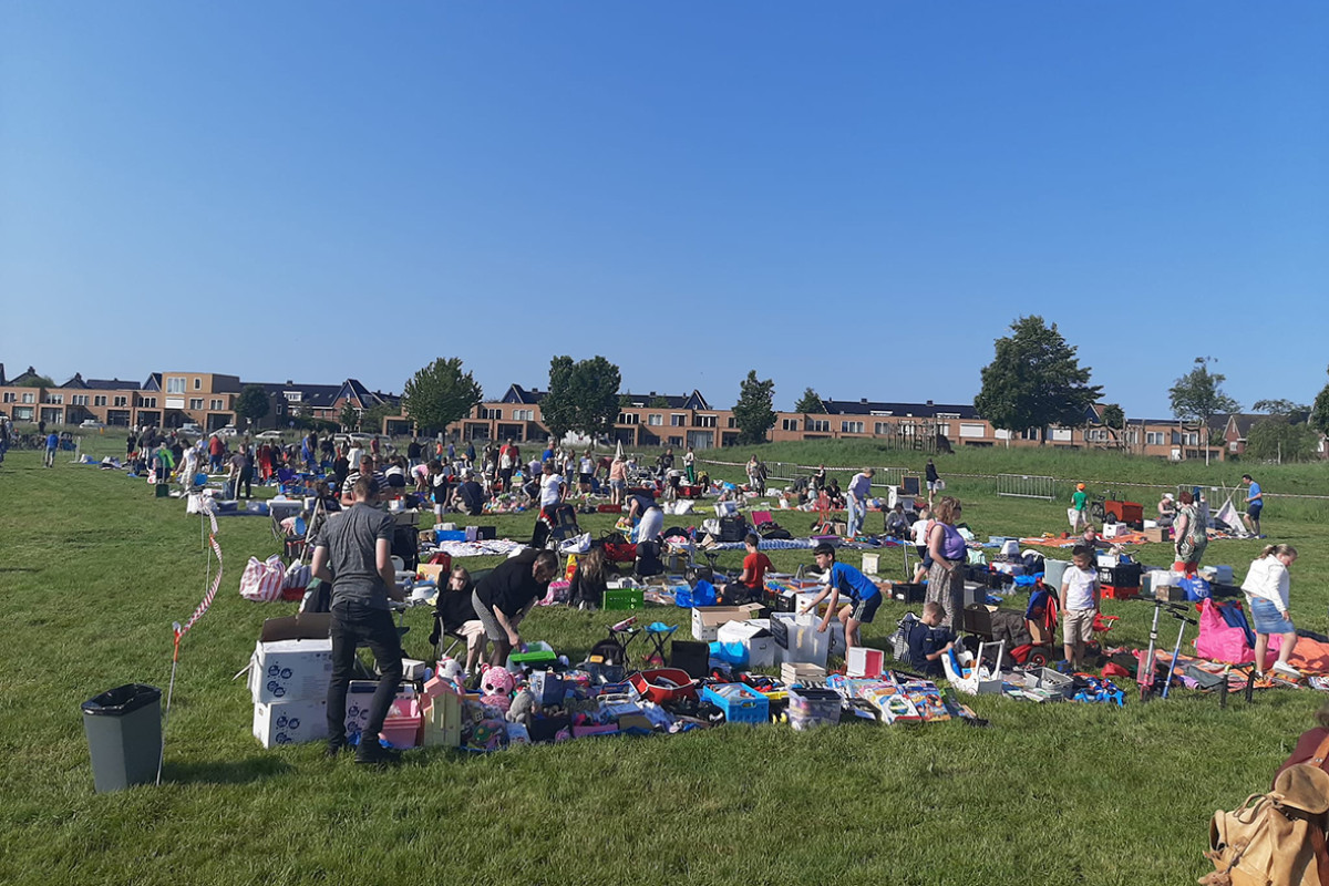 Groot grasveld waar kinderen op kleedjes spullen verkopen.