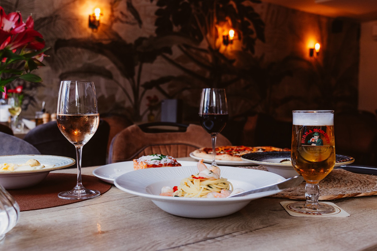 Borden met italiaans eten en twee glazen wijn en een biertje staan op tafel