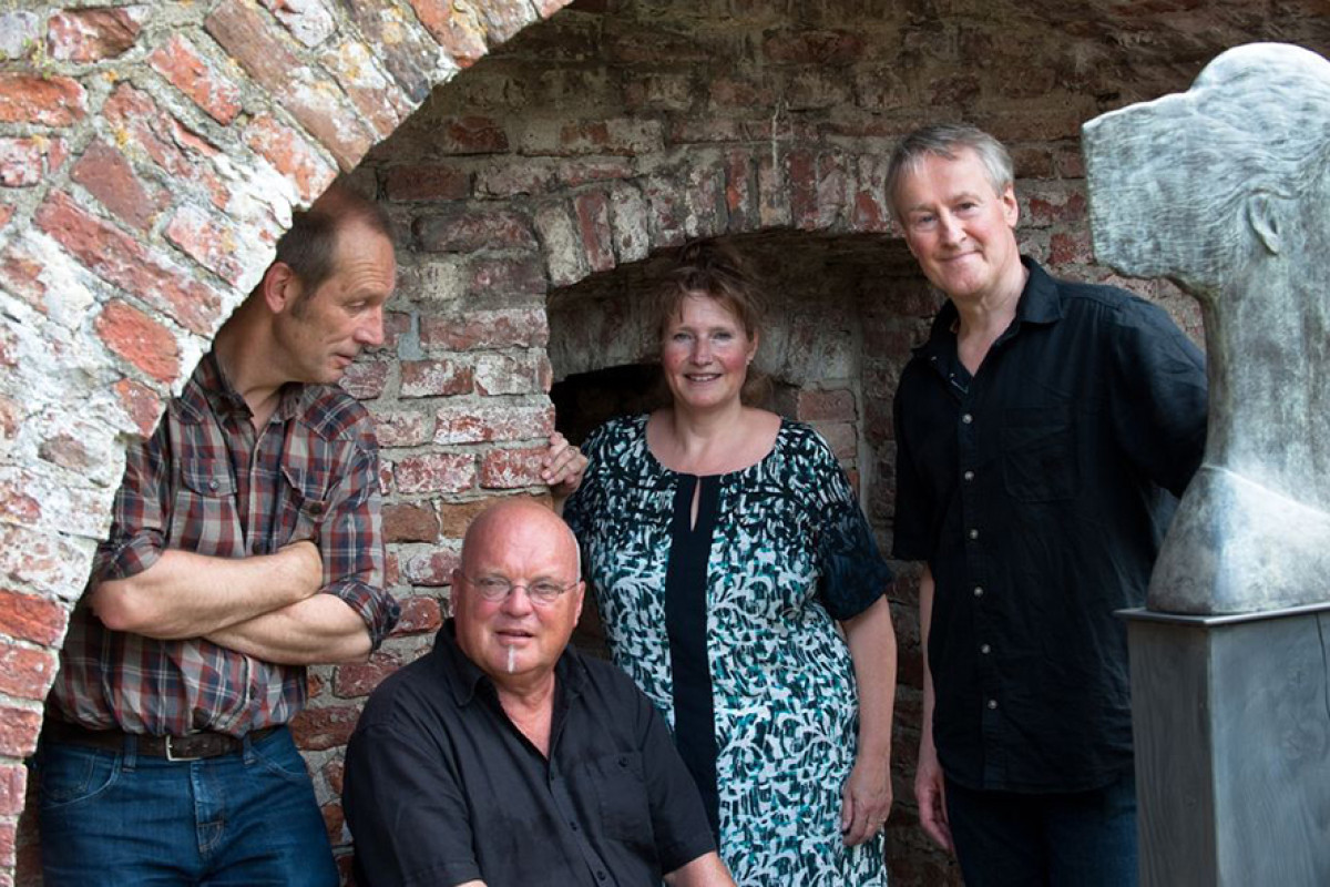 3 mannen en een vrouw staan onder een stenen boog