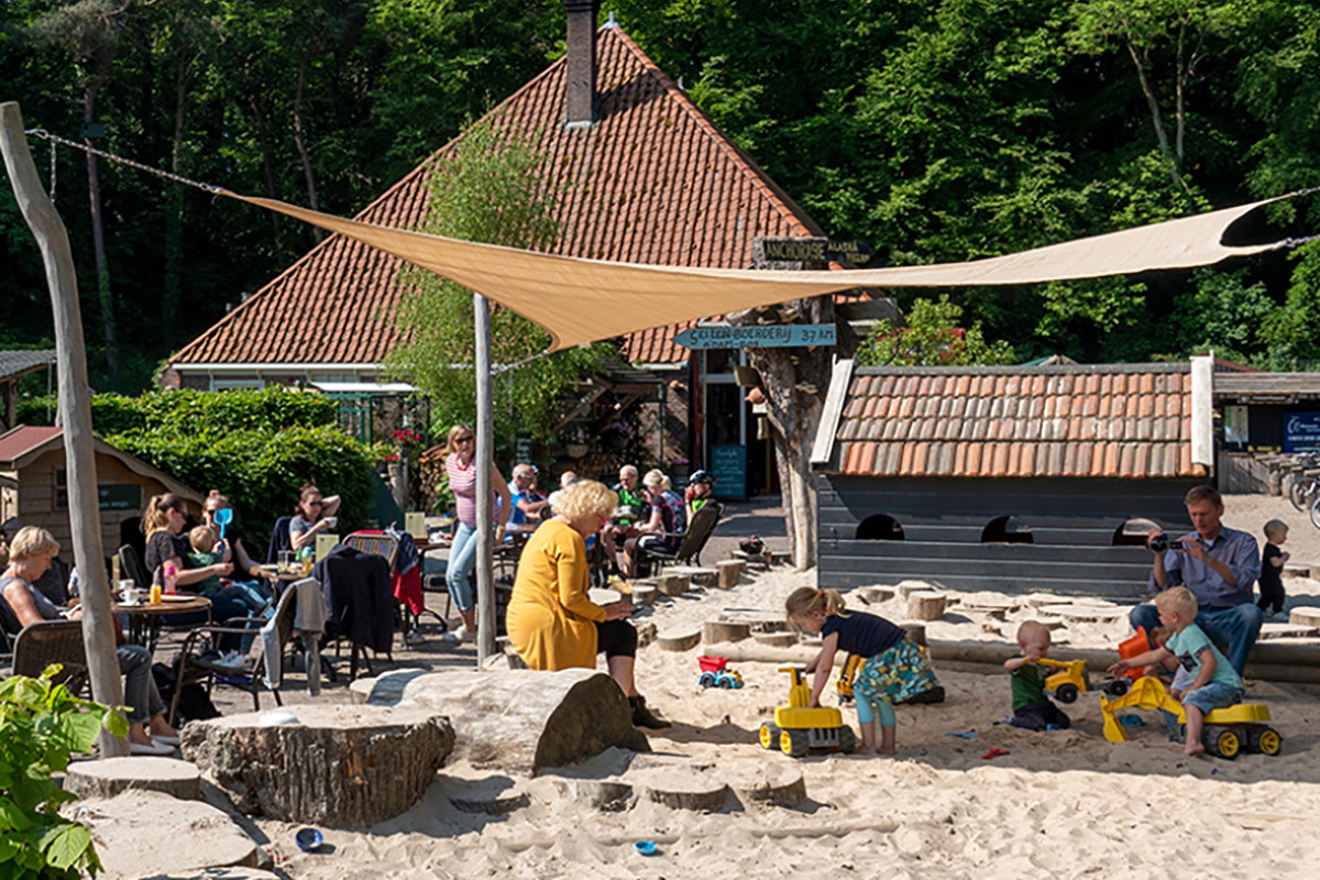 Zonnig terras van Gasterij Kruisberg met zicht op de zandbak waar kinderen in spelen.