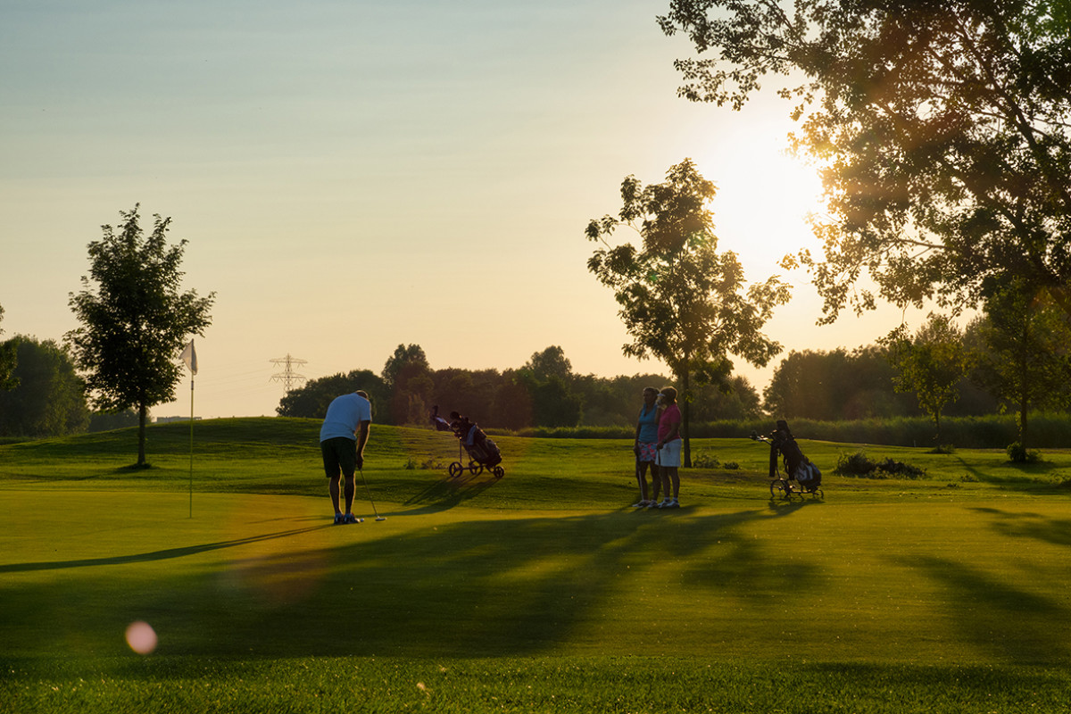 Zonsondergang op de golfbaan, met de laatste zonnestralen die de groene fairways en bunkers verlichten.