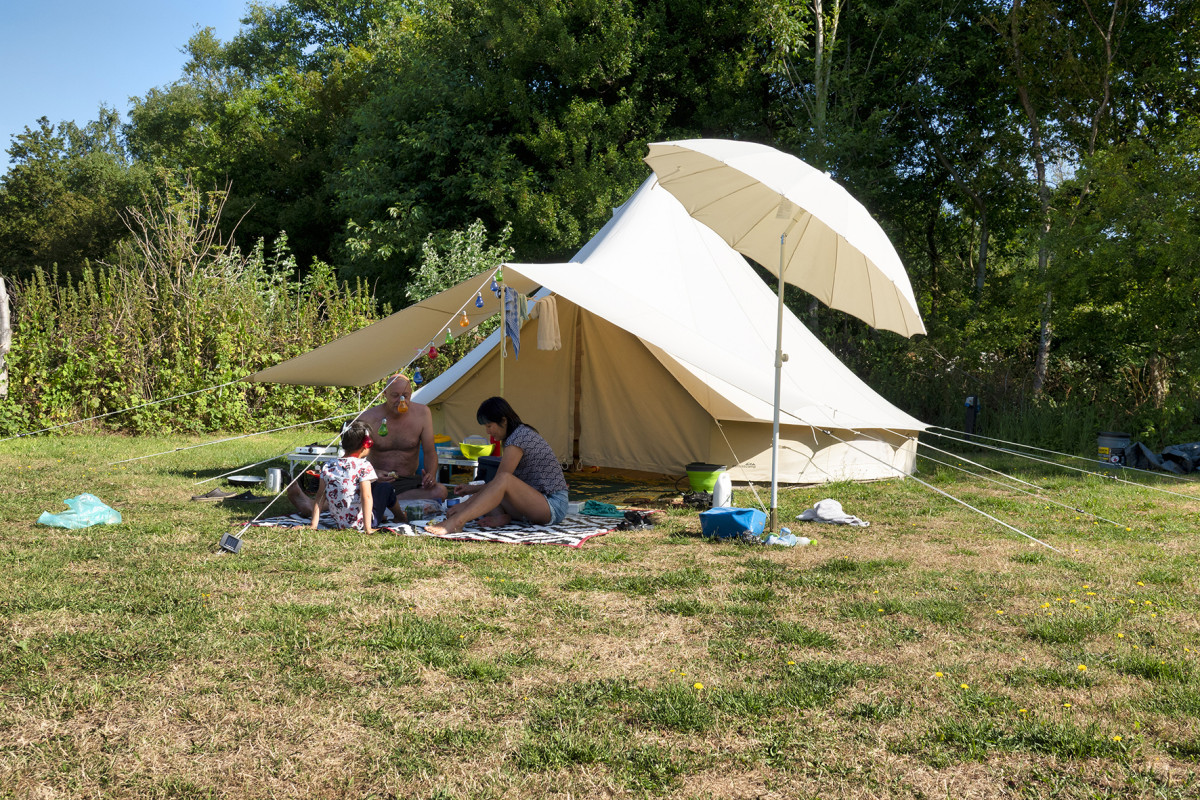 Lichte tent met parasol in groene omgeving.