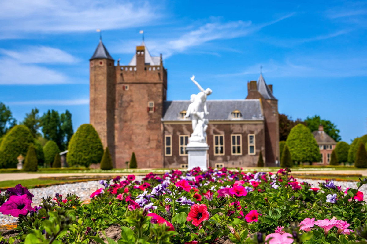 Zijaanzicht Slot Assumburg met blauwe lucht en roze bloemen op de voorgrond