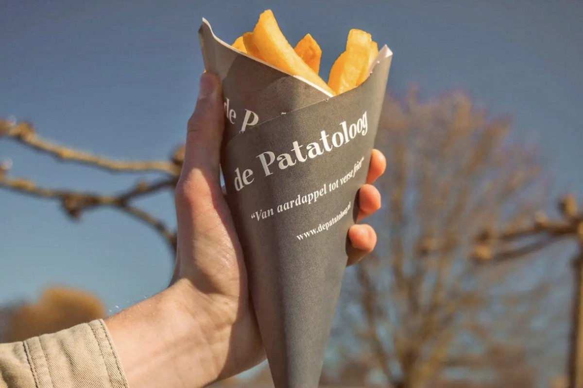 Een persoon houdt een zakje met frietjes van De Patatoloog vast.