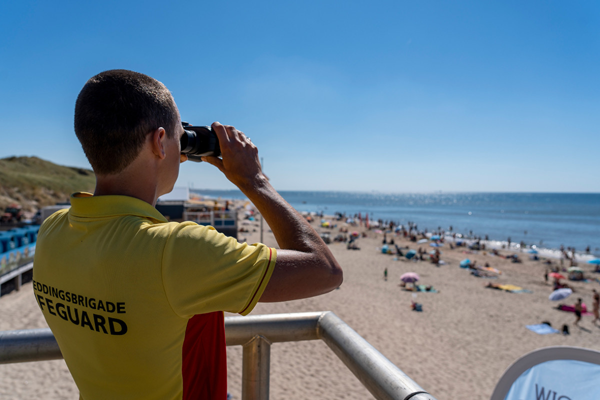 Reddingsbridgade kijkt vanaf een toren op het strand door een verrekijker naar zee.