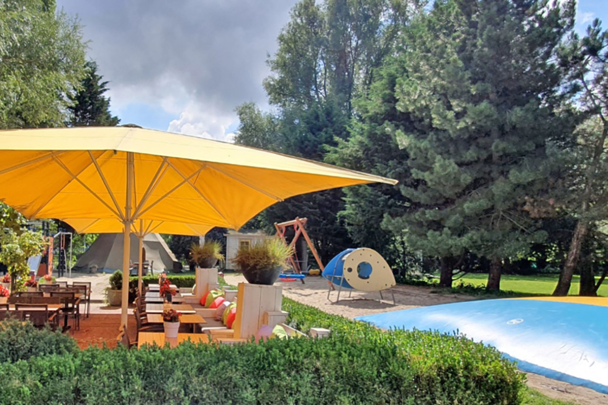 Terras van Restaurant Bleij met grote gele parasol en een deel van het springkussen.