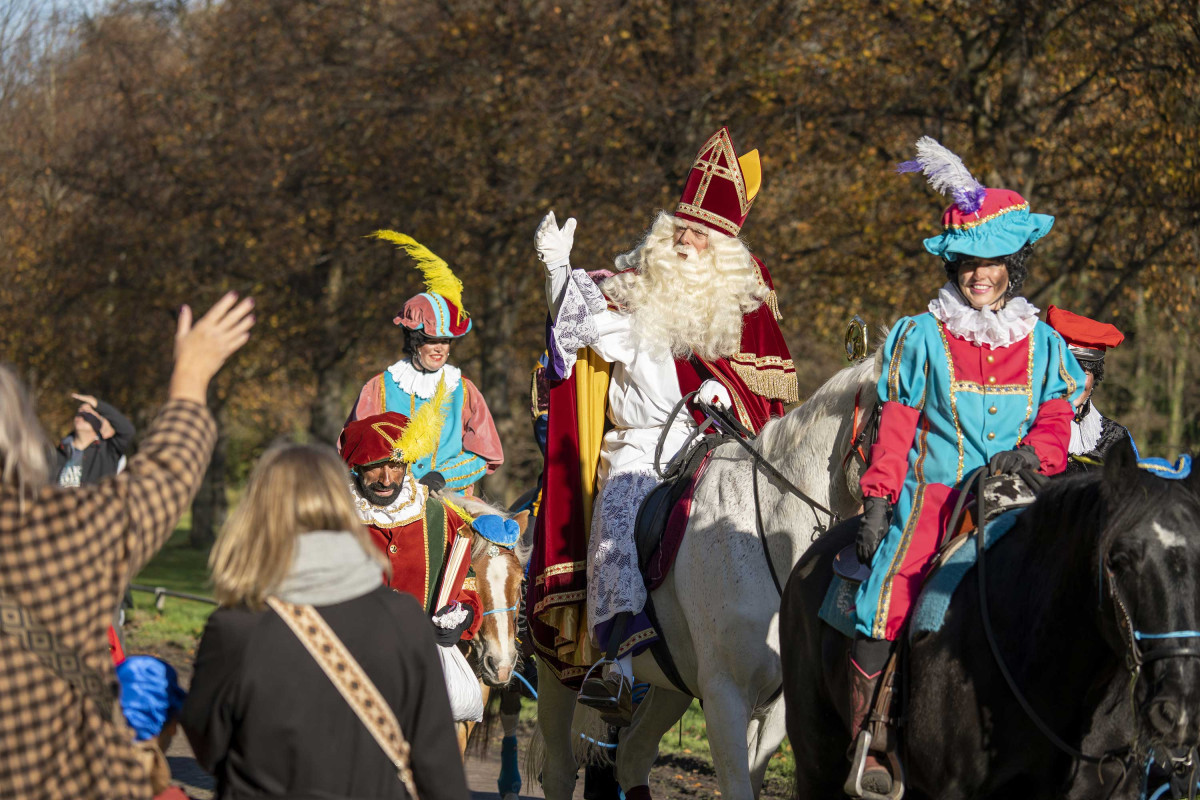 Sinterklaas op z'n paard met pieten erbij, zwaait naar mensen