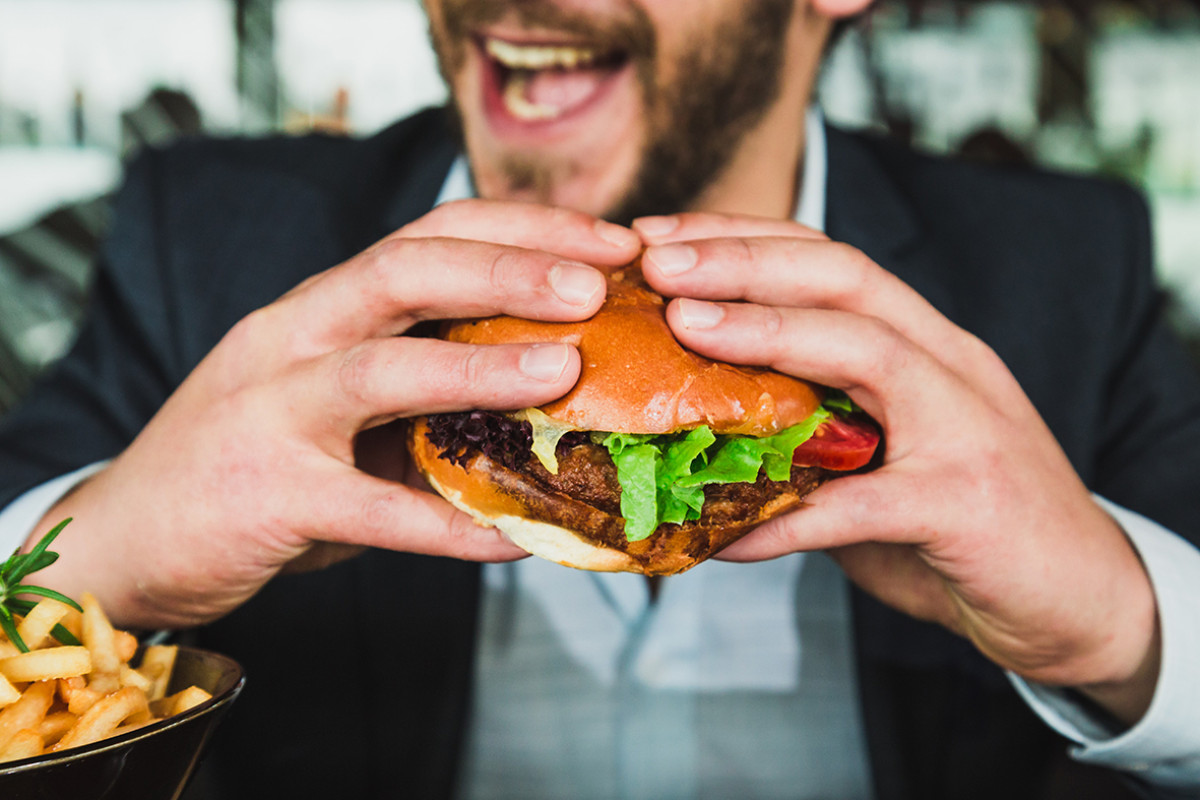 Man lacht en eet een hamburger met twee handen.