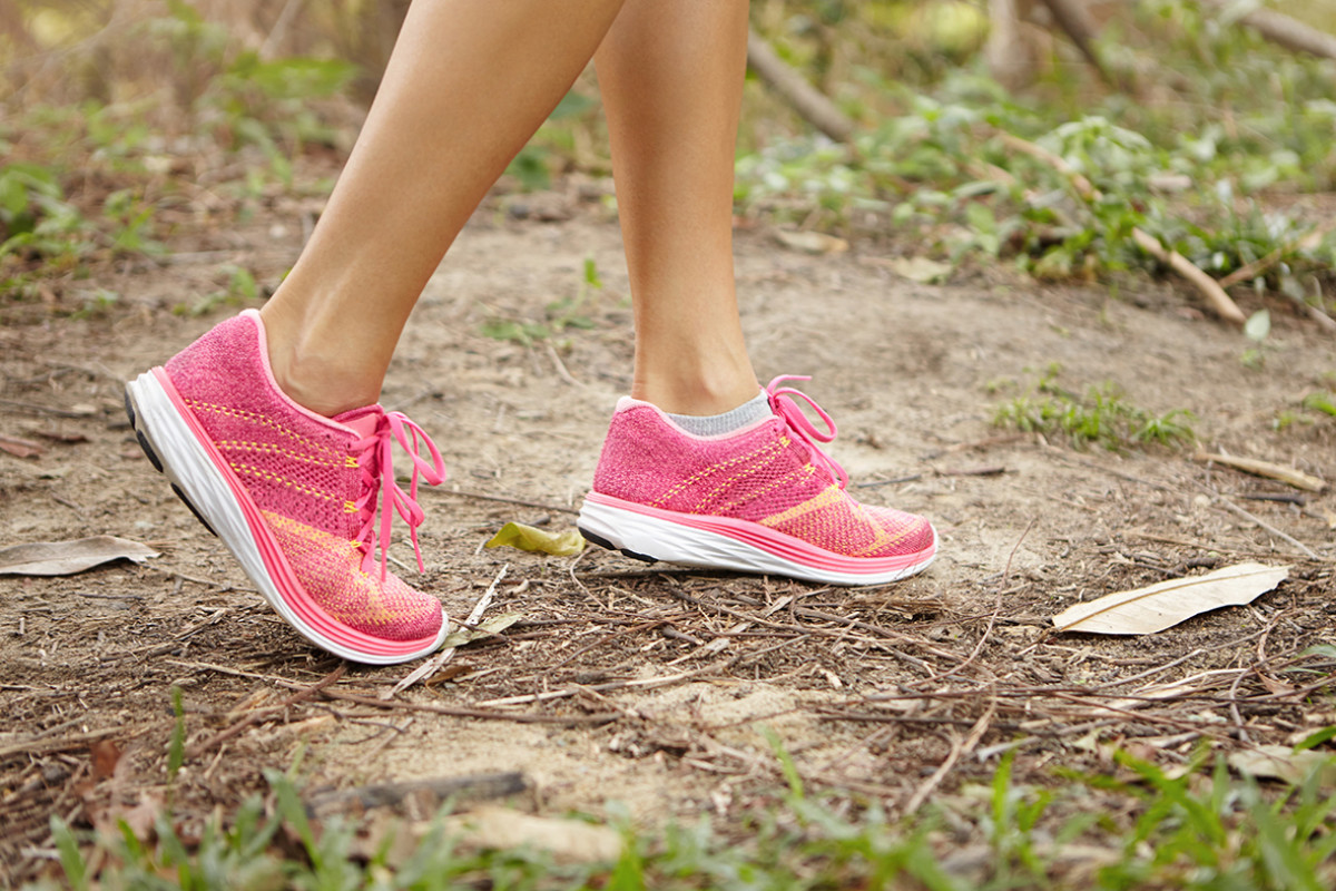 Vrouw met roze sneakers loopt over bospad