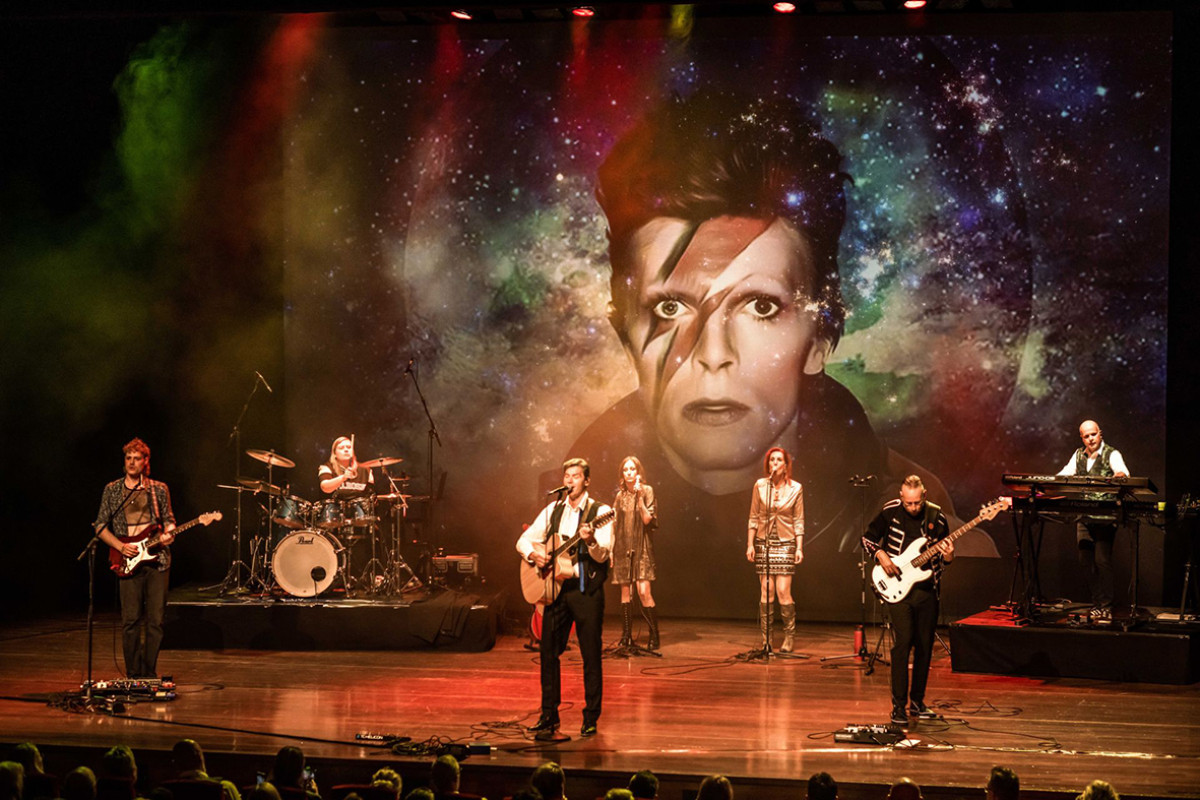 Band op podium met op de achtergrond een portret van David Bowie