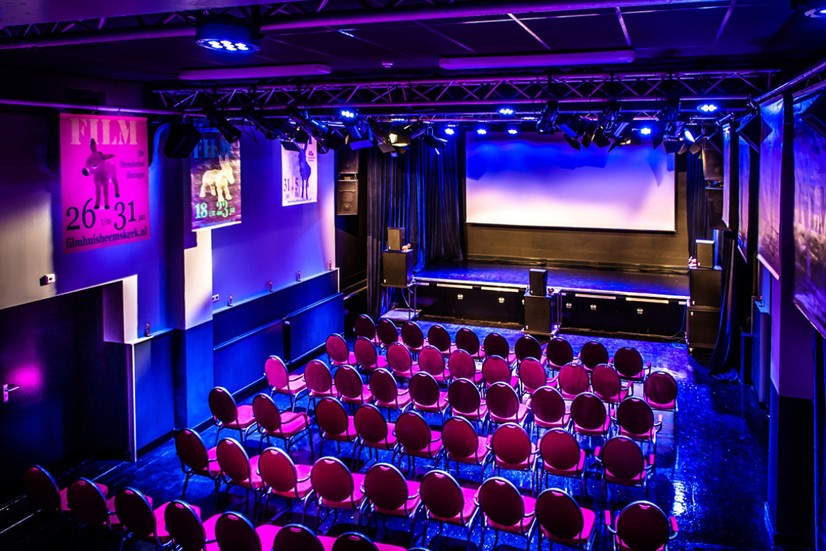 Een theaterzaal met paarse verlichting en stoelen.