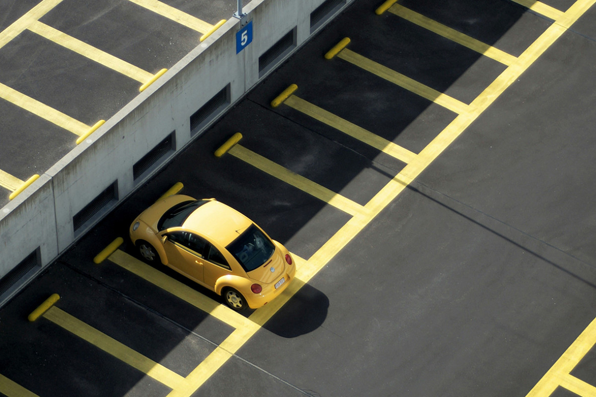 Gele auto geparkeerd in geel gemarkeerde parkeervak op zwart asfalt.